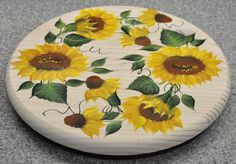 a wooden coaster with sunflowers painted on the front and sides, sitting on a gray surface