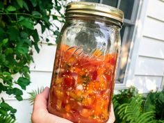 a person holding up a jar filled with red and yellow liquid in front of a house