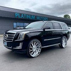 a black suv is parked in front of a dealership with white rims and chrome wheels