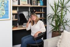 a woman sitting on a chair in front of a desk with a laptop computer and potted plant