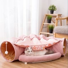 a cat is laying in a pink bed on the floor next to a chair and potted plant