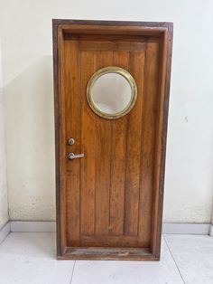 a wooden door with a porthole and mirror on the front, against a white wall