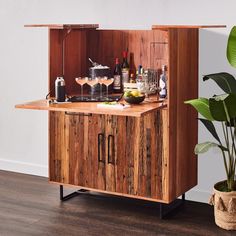 a wooden cabinet with wine glasses and bottles on it next to a potted plant