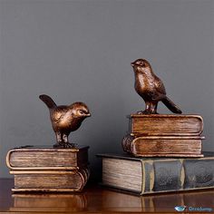 two bronze birds sitting on top of some bookends, one perched on the other