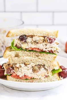 a white plate topped with a cut in half sandwich next to cherries and grapes