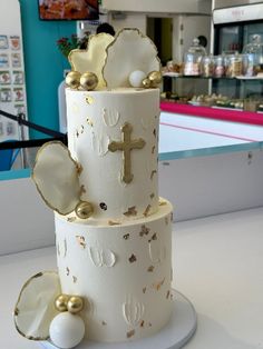 a three tiered cake decorated with gold and white decorations on a table in a bakery