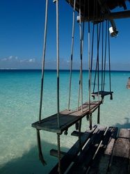 an empty dock in the middle of clear blue water with swings hanging from it's sides