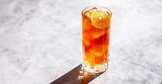 a tall glass filled with ice and orange slices on top of a white countertop