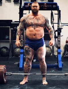 a man standing in front of a barbell with tattoos on his arms and legs