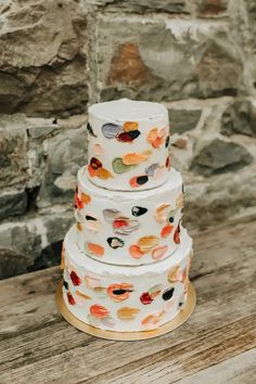 a three tiered wedding cake sitting on top of a wooden table next to a stone wall