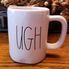 a white coffee mug with the word ugh written on it sitting on a wooden table