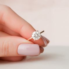 a woman's hand holding an engagement ring with a diamond in it, on a white background