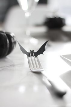 black and white photograph of a bat shaped fork on a table with wine bottle in the background