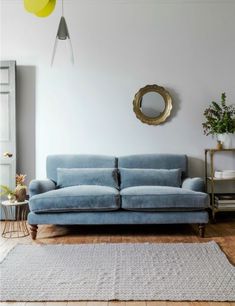 a blue couch sitting on top of a wooden floor next to a mirror and potted plant