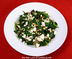 a white plate topped with spinach and feta cheese on top of a red table