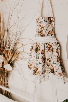 a flowered dress hanging on the wall next to a potted plant and dried grass