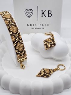 two pieces of jewelry sitting on top of a white cake next to a box with the words kris bliu handmade