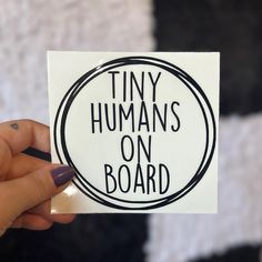 a person holding up a sticker that says tiny humans on board in black and white