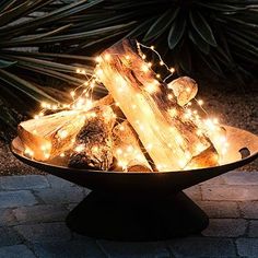 a bowl filled with lights and logs on top of a stone floor next to plants