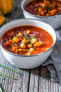 two bowls filled with soup sitting on top of a table next to bread and vegetables