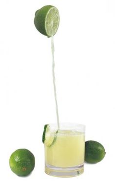 a lime being squeezed into a glass filled with lemonade and limes on the side