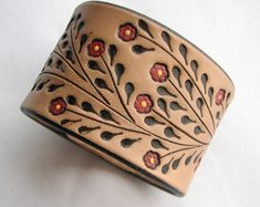 a brown leather bracelet with red flowers and leaves on it's side, sitting on a white surface