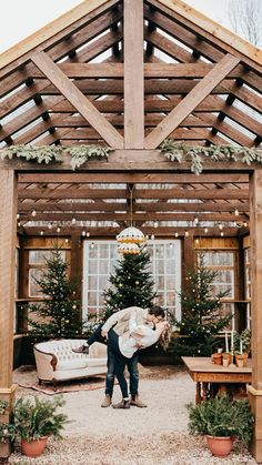 two people standing under a wooden structure holding each other