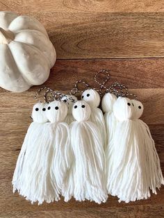 three white tasselled key chains with black eyes on them and two pumpkins in the background