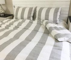 a bed with white and grey striped sheets on it's headboard, next to a night stand