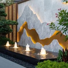 an outdoor fountain with lights in front of a wall that has mountains and trees on it