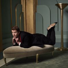 a man in a suit is laying on a couch with his feet up and hands under his chin