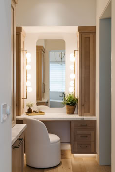 a white chair sitting in front of a bathroom vanity with lights on the wall above it