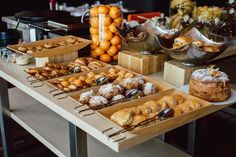 an assortment of pastries and desserts on display at a buffet table with oranges in the background