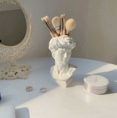 there is a statue with makeup brushes in it on the table next to a mirror