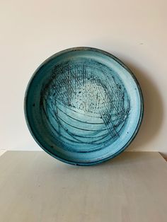 a blue bowl sitting on top of a wooden table in front of a white wall