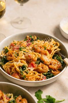 pasta with shrimp and spinach in a white bowl next to two glasses of wine