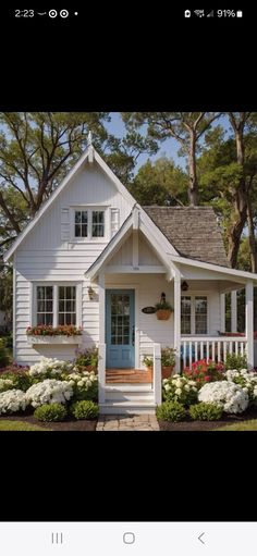 a small white house with blue door and flowers in the front yard on a sunny day