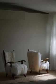 two chairs with sheepskin cushions sit in front of a window on a carpeted floor