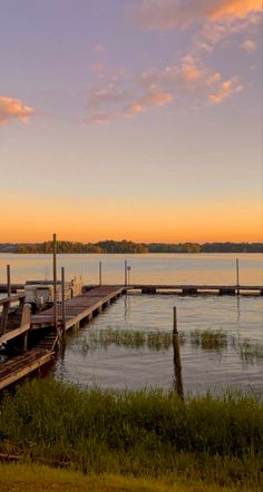 there is a boat dock on the water at sunset or dawn, with grass in front of it