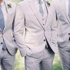 three men in suits and ties standing next to each other on the grass with their hands in their pockets