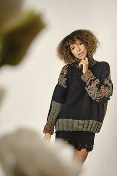 a woman standing in front of a white wall wearing a black sweater and lace shorts