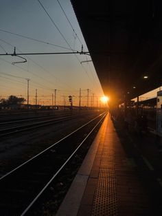 the sun is setting at an empty train station