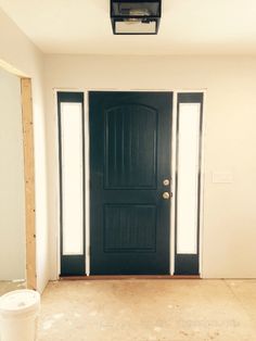 an empty room with a black door and two white buckets on the floor next to it