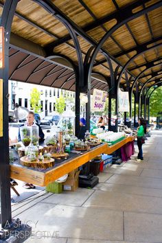 an outdoor market with people shopping and selling items on the tables in front of it