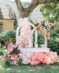 a wedding cake with balloons and flowers on the top is in front of a large tree