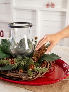 a person placing pine cones on top of a bowl filled with greenery and branches