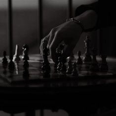 a person is playing chess on a table with other pieces in front of them and one hand reaching for the queen