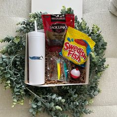 a box filled with snacks and condiments on top of a couch next to a cup