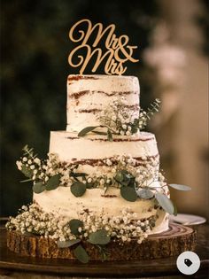 a three tiered wedding cake with greenery and mr and mrs sign on top