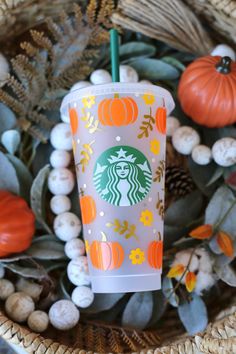 a starbucks cup sitting on top of a basket filled with leaves and pumpkins next to other fall decorations